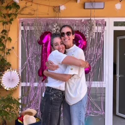 Two guests hugging in front of a pink balloon backdrop at a birthday party